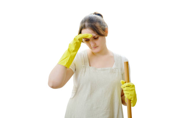 A sad woman holds her head with her hand while cleaning in a home kitchen, isolated on a white background