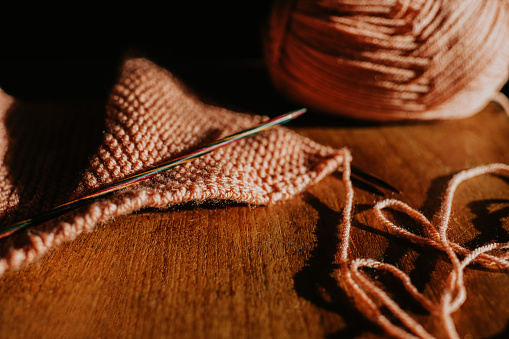 Close-up of a ball of pink wool, with a knitting needle inserted through the yarn. beside a knitting. Space for copy.