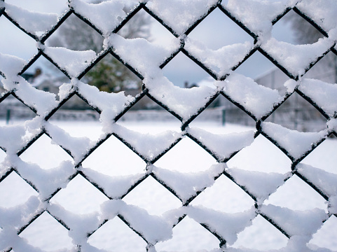 A snow-covered tennis court behind a wire mesh fence which is also decorated with snow.
