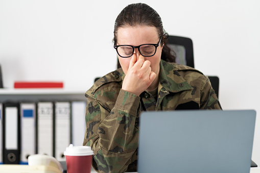Stressed female soldier working from home on laptop looking worried, tired and overwhelmed.