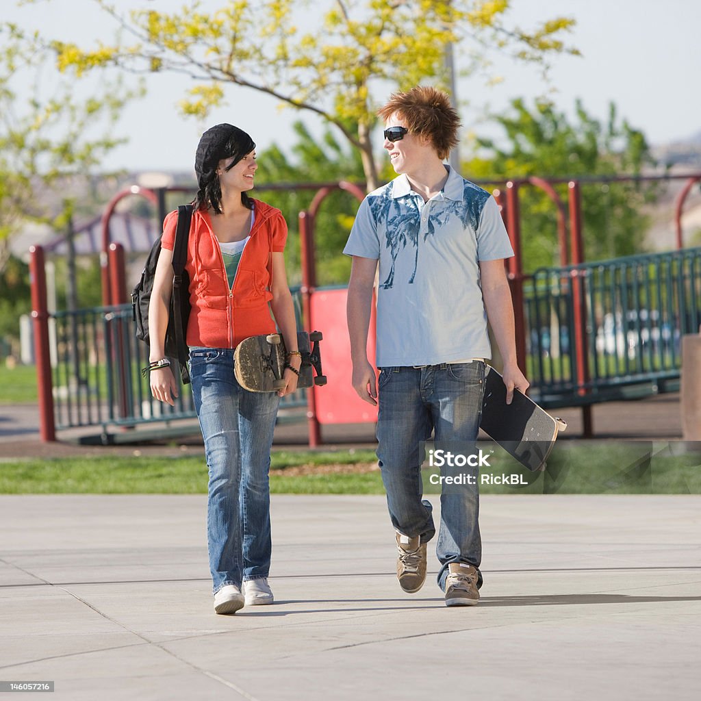 Teens couple walks Two kids walk home with skateboards through a park Boys Stock Photo