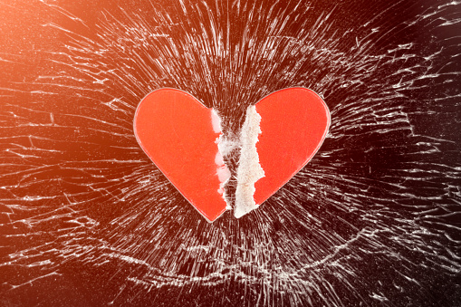 A torn red paper heart on a broken cracked black smartphone glass