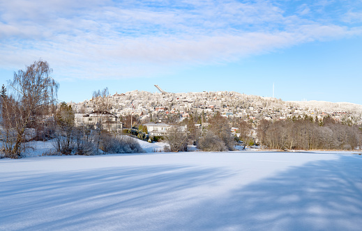 Ice covered lake with a snow covered hill called Holmenkollen in the background.