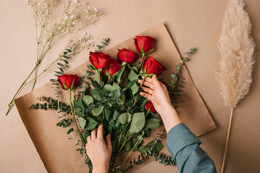 Hands making a bouquet with red roses on a natural background