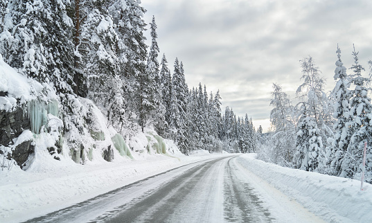 Icy road in a rural area with spruce tree forest and frozen water.