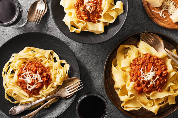 platos de tagliatelle fresco y pasta pappardelle con salsa boloñesa fresca y copas de vino tinto. sobre un fondo gris de piedra natural. vista superior. - pappardelle fotografías e imágenes de stock