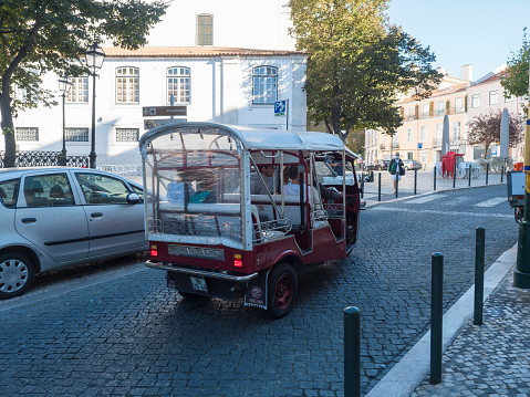 Lisbon, Portugal, October 24, 2021: View of red tuk-tuk, Mototaxi popular tourist transportation in Lisabon streets, small vehicles called Tuk Tuk, driving on three wheels.