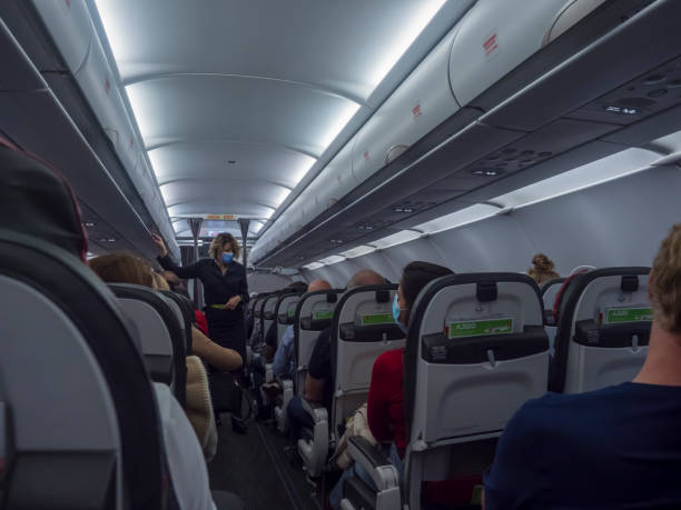 interior of commercial tap airline airplane, passengers sitting on the economy class seats and stewardess wearing the face mask - tap airplane imagens e fotografias de stock
