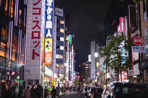 Shot of a Japanese shopping district with many neon advertisements and lights turned on. There is a crowd of people walking along the street at night.