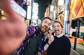Portrait Of A Caucasian Couple Making A Selfie While Enjoying Street Food Together At Japan