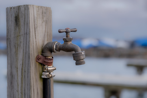 Photo of an outside water spigot, hose bib, on a wooden post.