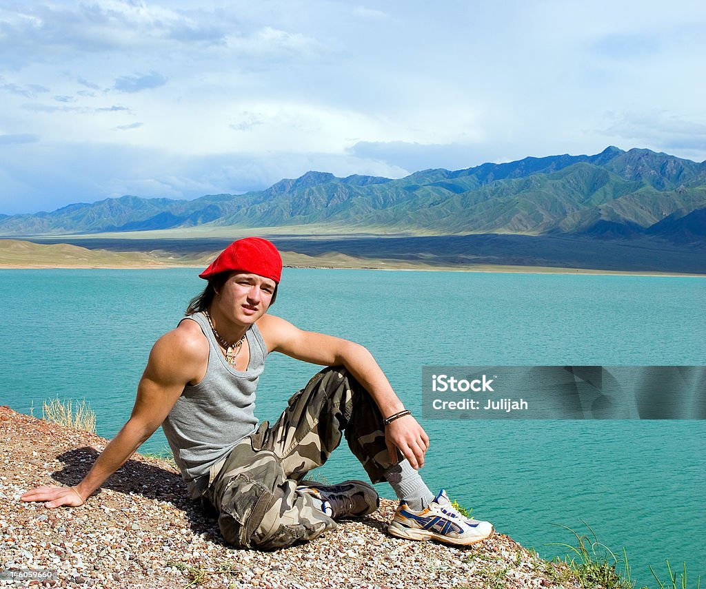 Garçons adolescents assis par un superbe lac de l'eau verte - Photo de Assis libre de droits