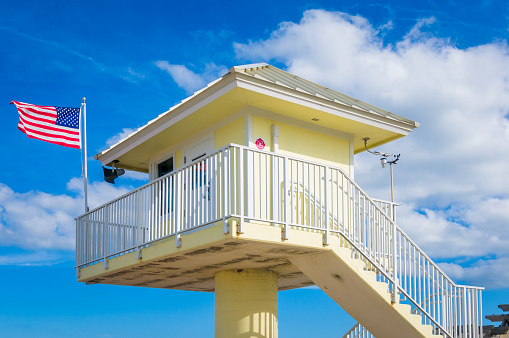 Ormand Beach, Florida, USA-January 3, 2023- The American flag flies over a bright yellow lifeguard tower stands high over Ormand Beach guarding and protecting the beachgoers and shore fishermen who use this area.