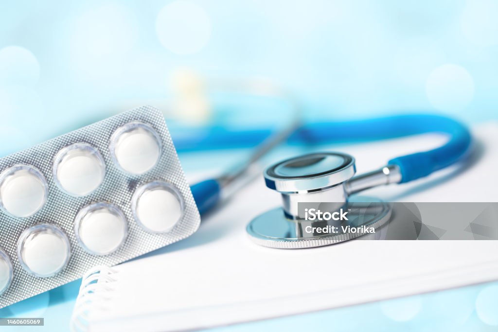 Medical concept - stethoscope with some pills on a spiral notebook Close-up of a stethoscope with some pills on a spiral notebook. Defocused lights bokeh background, space for copy. Shallow depth of field. Pill Stock Photo