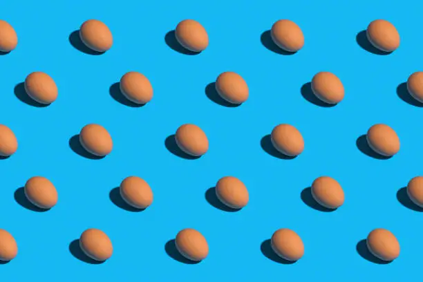 Overhead view of brown eggs in rows on a bright blue background