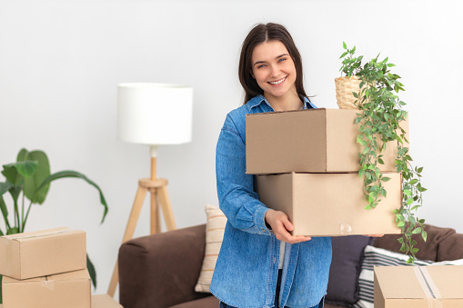 Happy young woman moving into her new home. Beautiful female student holding cardboard boxes, moving to your room in a student dorm or to a new rented apartment