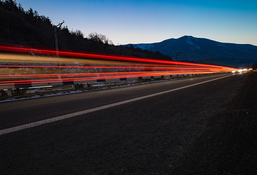 Light traces of passing cars with a mountain partially covered by snow, at dusk in winter