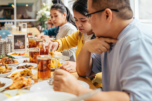 Group of mixed aged relatives sitting at dining table enjoying nasi padang (minangkabau food) talking and laughing, togetherness, healthy eating, meal time, domestic life