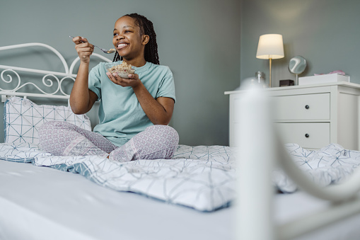 A young woman is eating breakfast at home and enjoying in bedroom