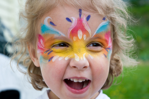 A young girl with face paints makes a face at the camera
