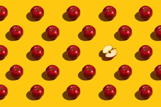 Overhead view of rows of shiny red apples with one cut in half on a bright yellow background