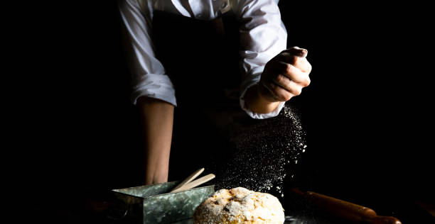 istock Fresh bread and Chef hands with falling flour on black background. 1460613325