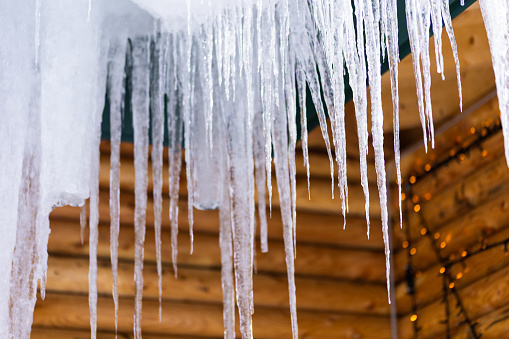 Long icicles slowly drip down and hang from a log cabin roof.