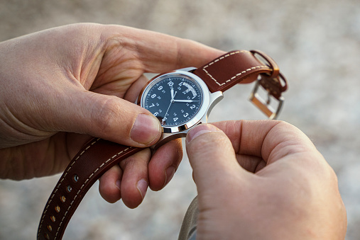 Close up of a man adjusting the his wristwatch with a browns leather strap