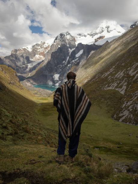 Young male hiker in traditional poncho at Cordillera Huayhuash Circuit andes mountain Gangrajanca lake Ancash Peru stock photo