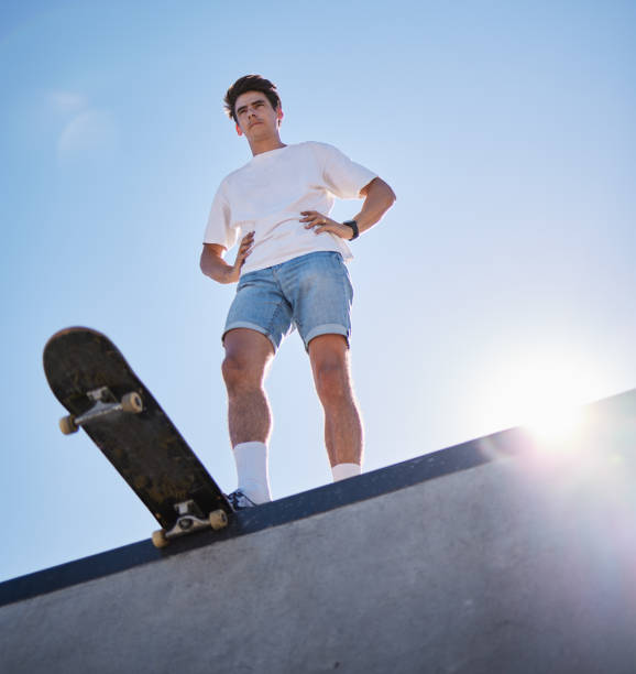 cielo azul, monopatín y joven desde abajo en la rampa de skate listo para el truco. fitness, moda callejera y deportes urbanos, un skater en skatepark y sol de verano para la aventura, la libertad y el deporte extremo. - vertical ramp fotografías e imágenes de stock