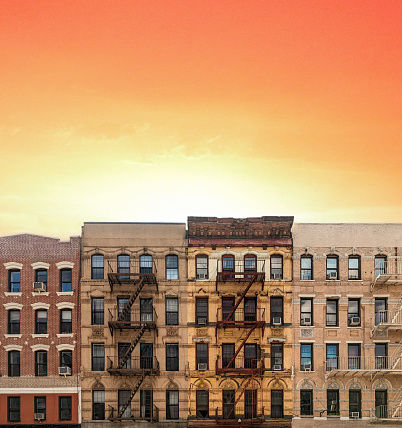 Old New York City style brick apartment buildings with empty sky above with orange and yellow glow of sunset