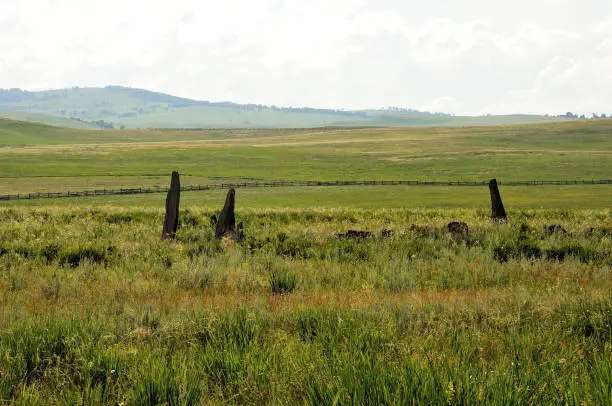Photo of Ancient burial stones enclosed by a wide fence in the center of the picturesque steppe at the foot of high hills.