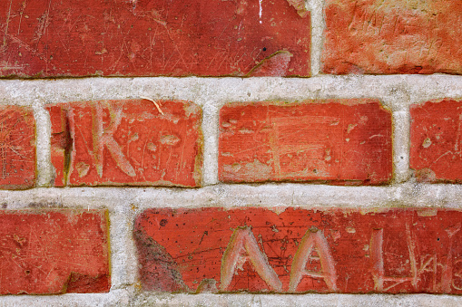 Very old and abandoned school with brick walls marked by letters, dates, and signs made by school children.\nOld red brick wall grunge texture. Old cracked bricks wall with a weathered surface. Brick wall background, copy space for design and text. Vintage brick wall.