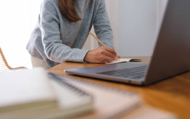 istock Closeup image of a young woman writing on notebook while working or study on laptop computer at home 1460654922