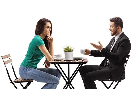Young woman sitting at a wooden table and listening to a businessman isolated on white background