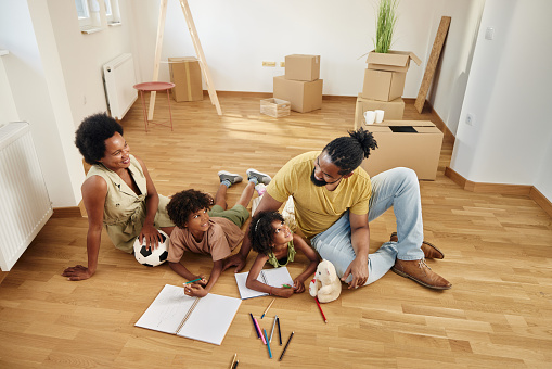 Happy parents and their small kids talking while having a creative time on the floor after relocating into new home. Copy space.