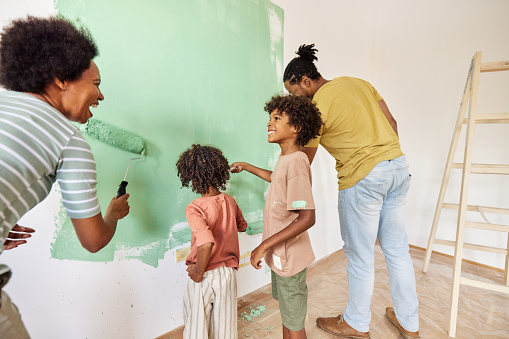 Happy black parents and their small kids communicating while painting their walls during home renovation process. Copy space.