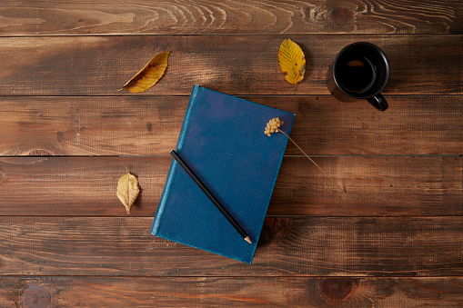 Pencil and book wooden background with cup of coffee and autumn leaves.