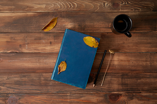 Pencil and book wooden background with cup of coffee and autumn leaves.