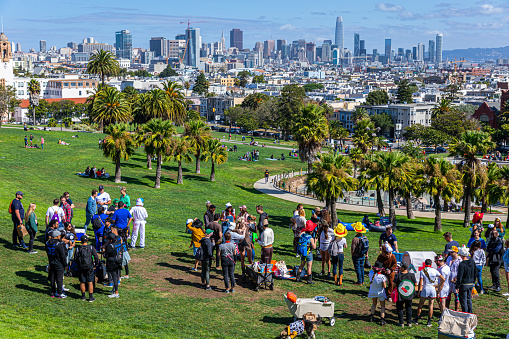 San Francisco, California, USA - September 29, 2019: People relax and enjoy outdoor activities at green recreation on hill slope of Mission Dolores park with background of city.