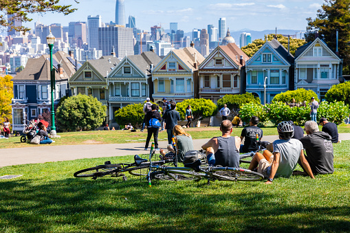 San Francisco, California, USA - September 29, 2019: People enjoying outdoor activities and view of Painted Ladies houses in Alamo Square with background of city in autumn.