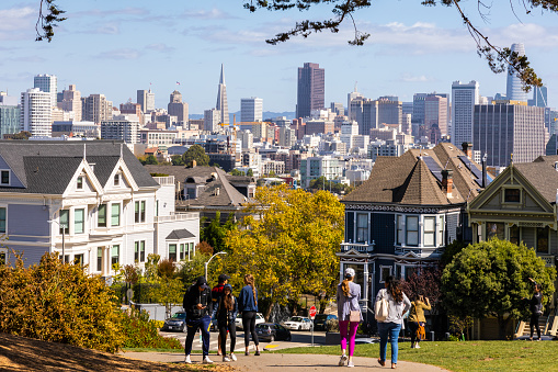 San Francisco, California, USA - September 29, 2019: People enjoying outdoor activities and view of Painted Ladies houses in Alamo Square with background of city in autumn.