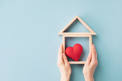 Womans hands holding model of wooden house with red heart for happy family. Real estate, sweet home, housewarming, mortgage and buy new property minimal concept.