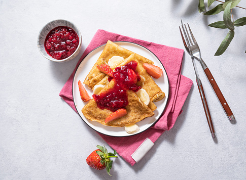Sweet pancakes with berry jam, strawberries and banana on a light background. The concept of homemade healthy food. Top view and space for text.