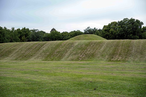 Native American Hopewell Culture prehistoric Earthworks burial mounds in Mound City park Ohio. Ancient circular mounds and long mound in the foreground. Grass is neatly trimmed with trees and dramatic sky.