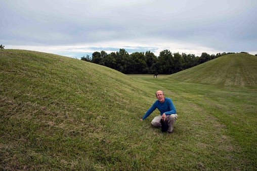 Native American Hopewell Culture prehistoric Earthworks burial mounds in Mound City park Ohio. Ancient circular mounds and long mound in the background. Grass is neatly trimmed with trees and dramatic sky.