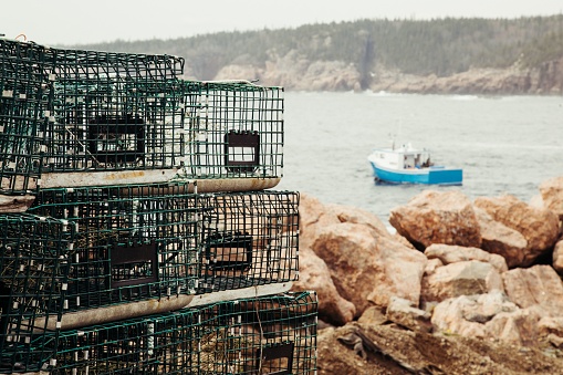 A beautiful view of a rocky coast with crab cages on it against an ocean with a boat on it