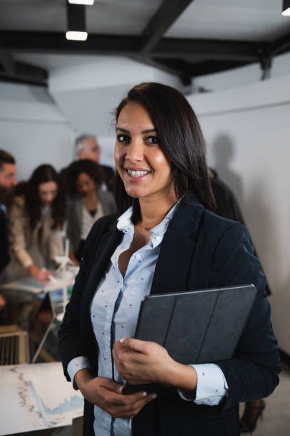 istock Vertical portrait elegant businesswoman smiling while looking at camera holding digital tablet. Colleagues working in office. 1460716842