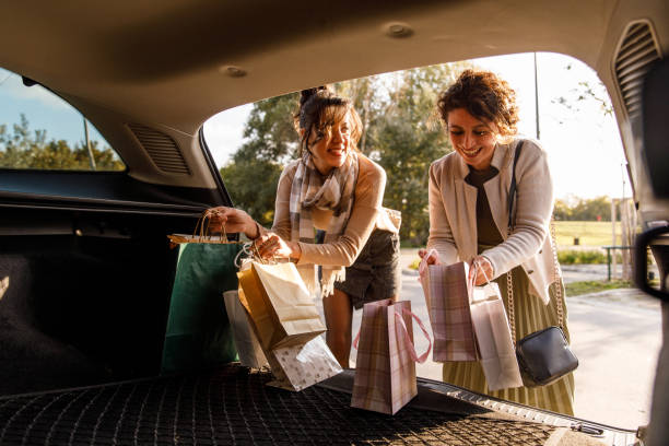 Candid shot of two cheerful women having bonding moments and laughing together while loading shopping bags in the car trunk.