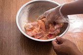 Close-up shot of raw chicken being mixed with marinade in a bowl by a person